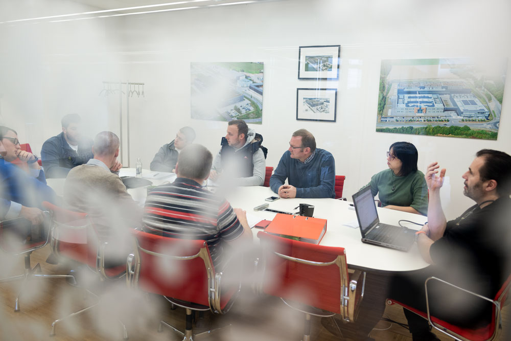 Through a glass front you can see a table where several people sit together in a team and discuss topics.